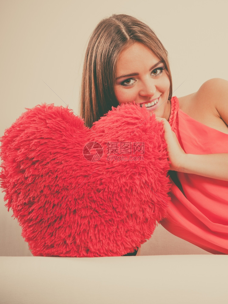 在白沙发上坐着带红色的心形枕头微笑着可爱的年轻女孩情人节的爱图片