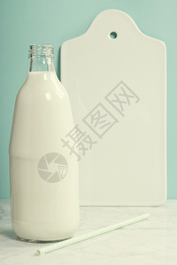 一瓶牛奶白陶瓷服务板和大理石桌上的纸草蓝底美味有营养和健康的奶制品图片
