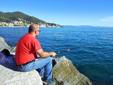 在岩石上捕鱼的渔民图片