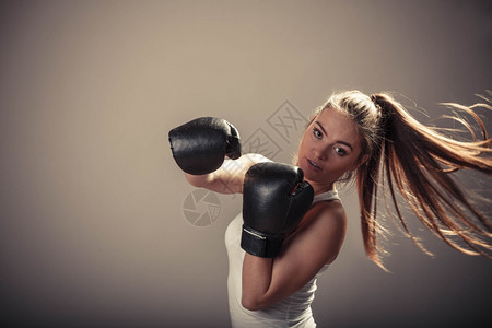 精力充沛的年轻女子用拳击手套打架与对手拳击运动和体力建设强健的年轻女子打敌有马尾的女子戴白箱顶和拳击手套背景图片