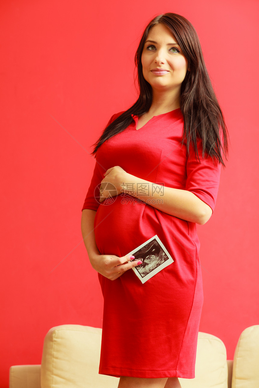 怀孕母亲和幸福身着优雅红礼服的孕妇肚子室内手头超声波扫描图片