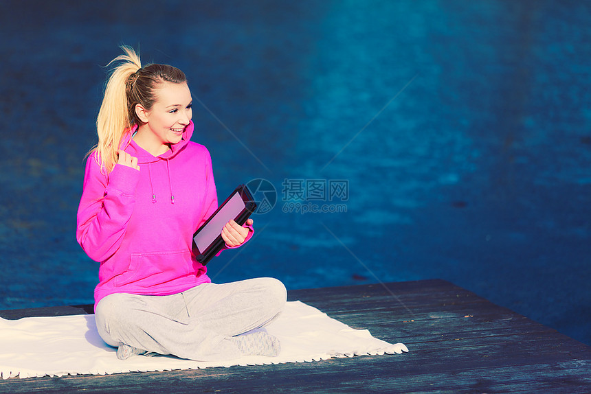 坐在公园的年轻女孩从平板上学习瑜伽注意健康的生活方式和微弱的身材使用技术的体育运动图片