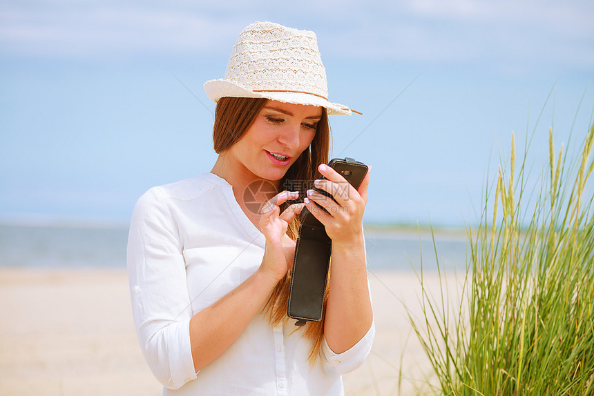 女孩在沙滩上用智能手机发短信交流概念年轻女在夏季沙滩上用智能手机发短信女孩使用手机图片