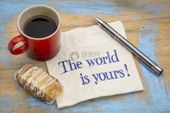 世界是你的一个积极肯定用笔咖啡杯和饼干在餐巾纸上用笔咖啡和饼干对着涂黑的木头纸巾上写字图片