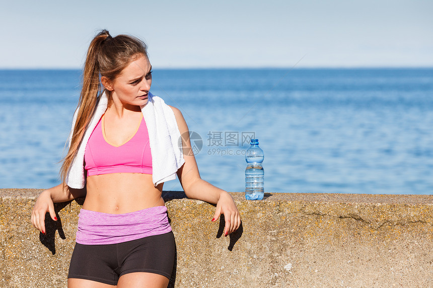 穿运动服的妇女休息从塑料瓶中补充饮用水休息后在海边户外运动锻炼后休息图片