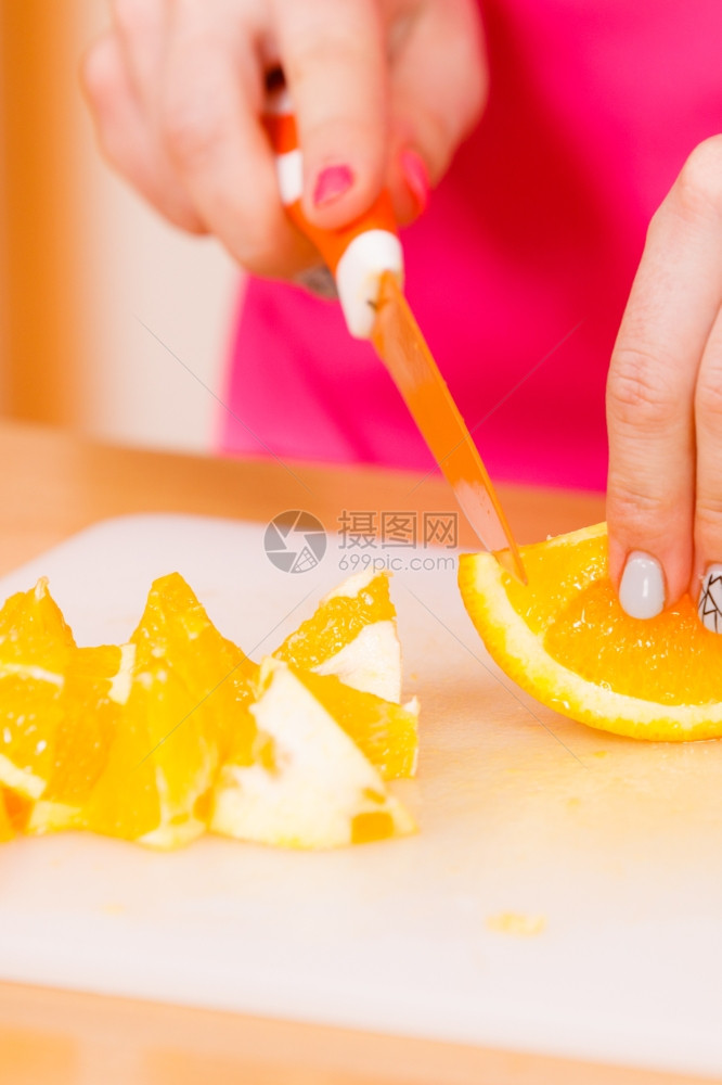 在家厨房的年轻女家庭主妇在切菜板上开新鲜橙子水果用于沙拉或多汁图片