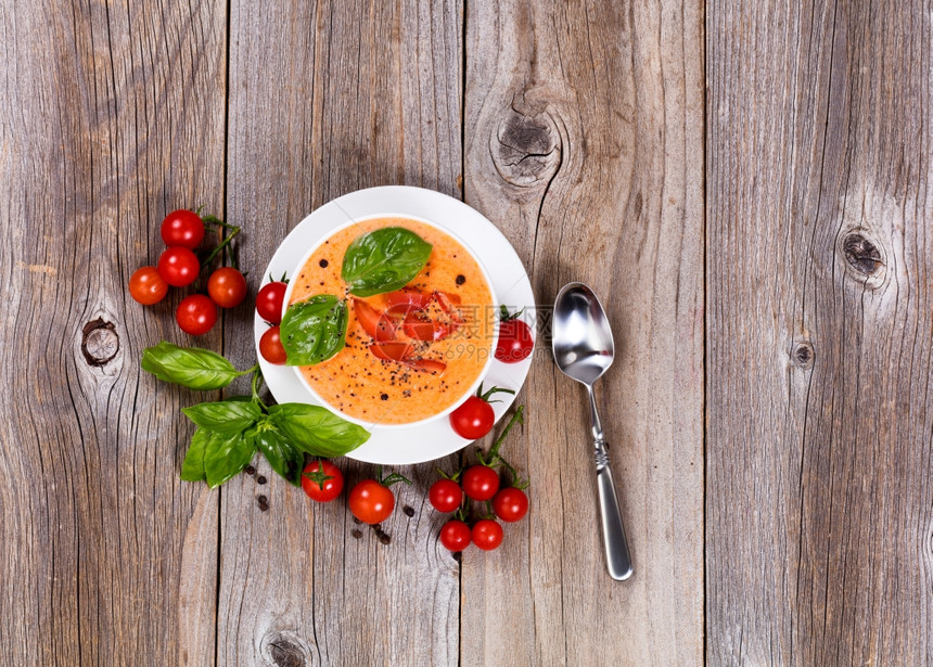 白色碗里新鲜的奶油番茄汤上面有樱桃西红柿和竹木板上的烤肉图片