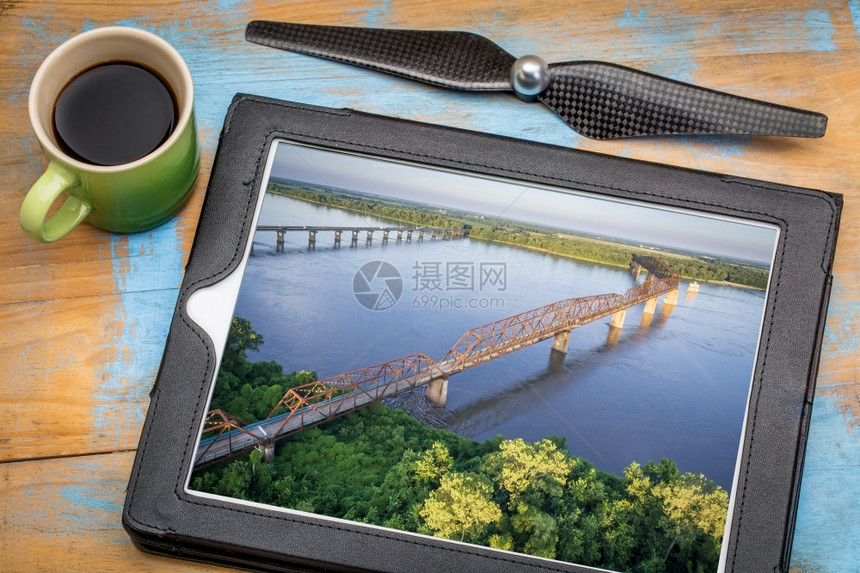 由摄影师在数字平板上用无人机螺旋推进器和咖啡审查密西比河里弗上空新旧岩桥链的中图片图片