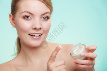 美容治疗女在脸上涂润湿奶油持有皮肤护理产品的罐子绿蓝背景摄影棚拍背景图片