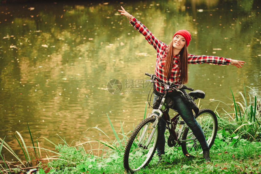 年轻女子骑着自行车在公园水潭边比划手势图片