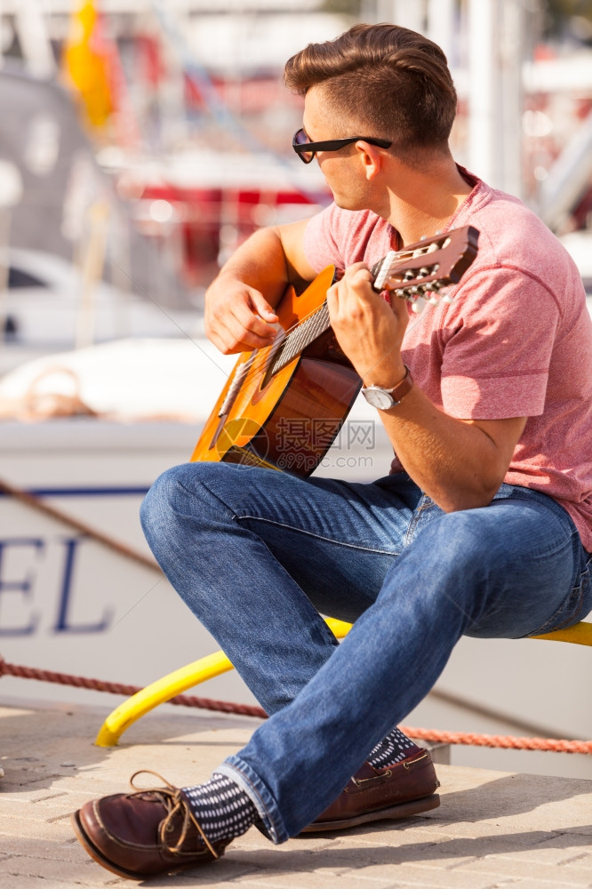年轻人弹吉他浪漫音乐声男化的概念年轻人弹吉他男孩坐在码头玩乐器图片