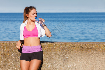 穿运动服美女在海边喝水休息图片