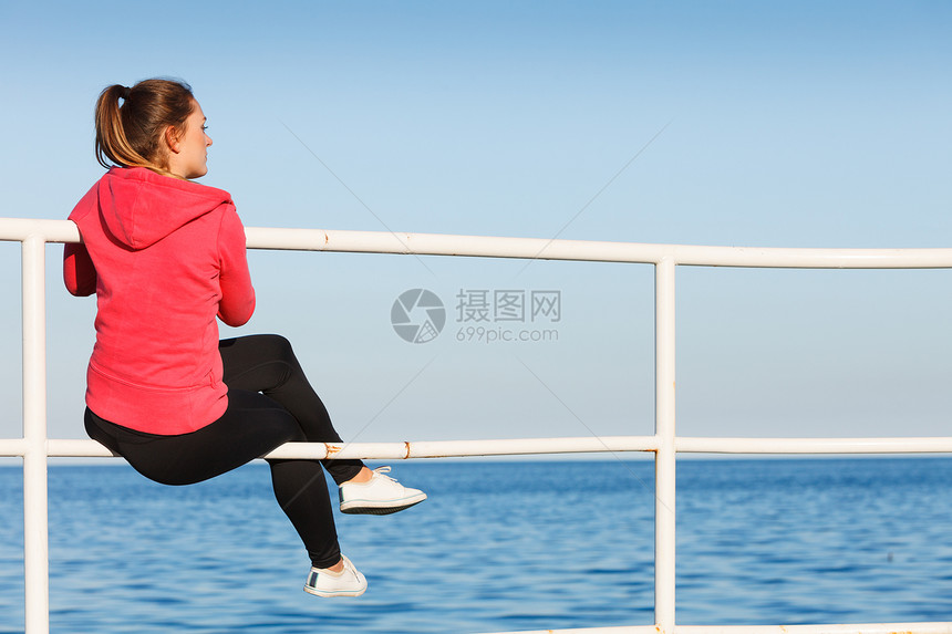 坐在码头上看地平线户外的妇女在运动后休息的妇女穿着运动服坐在码头上放松地平线后视的健身女坐在码头上看地平线后视的美貌女孩坐在码头图片