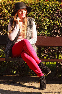 穿着时尚服装的华丽髦年轻女子穿着黑帽坐在公园长椅上的女孩肖像图片