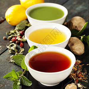 茶叶概念陶瓷碗和木制背景原料中不同种类的茶叶黑绿色和红背景图片