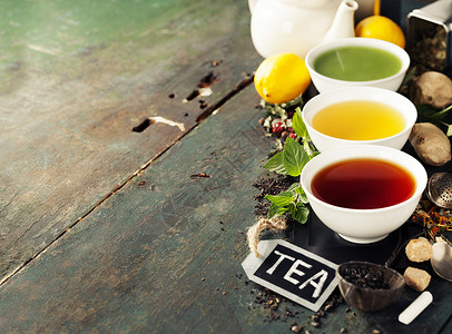 茶叶概念陶瓷碗和木制背景原料中不同种类的茶叶黑绿色和红背景图片