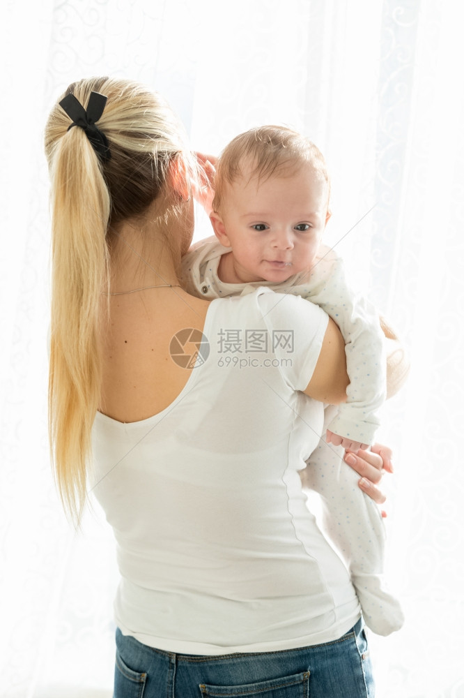 美丽的年轻女子肖像与她三个月大的男婴在窗户上图片