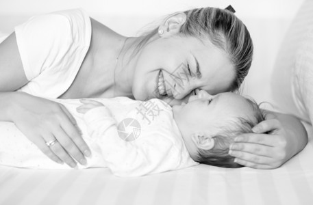 快乐的母亲拥抱和在床上吻她的孩子黑白画像图片