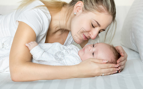 美丽年轻母亲抱着婴儿男孩躺在床上的近身肖像图片