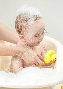 父与子洗澡与黄橡皮鸭在泡沫浴中玩耍的可爱小男孩肖像背景