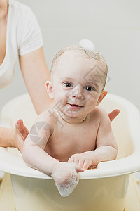 坐在浴缸里看着摄像机的可爱笑婴儿肖像图片