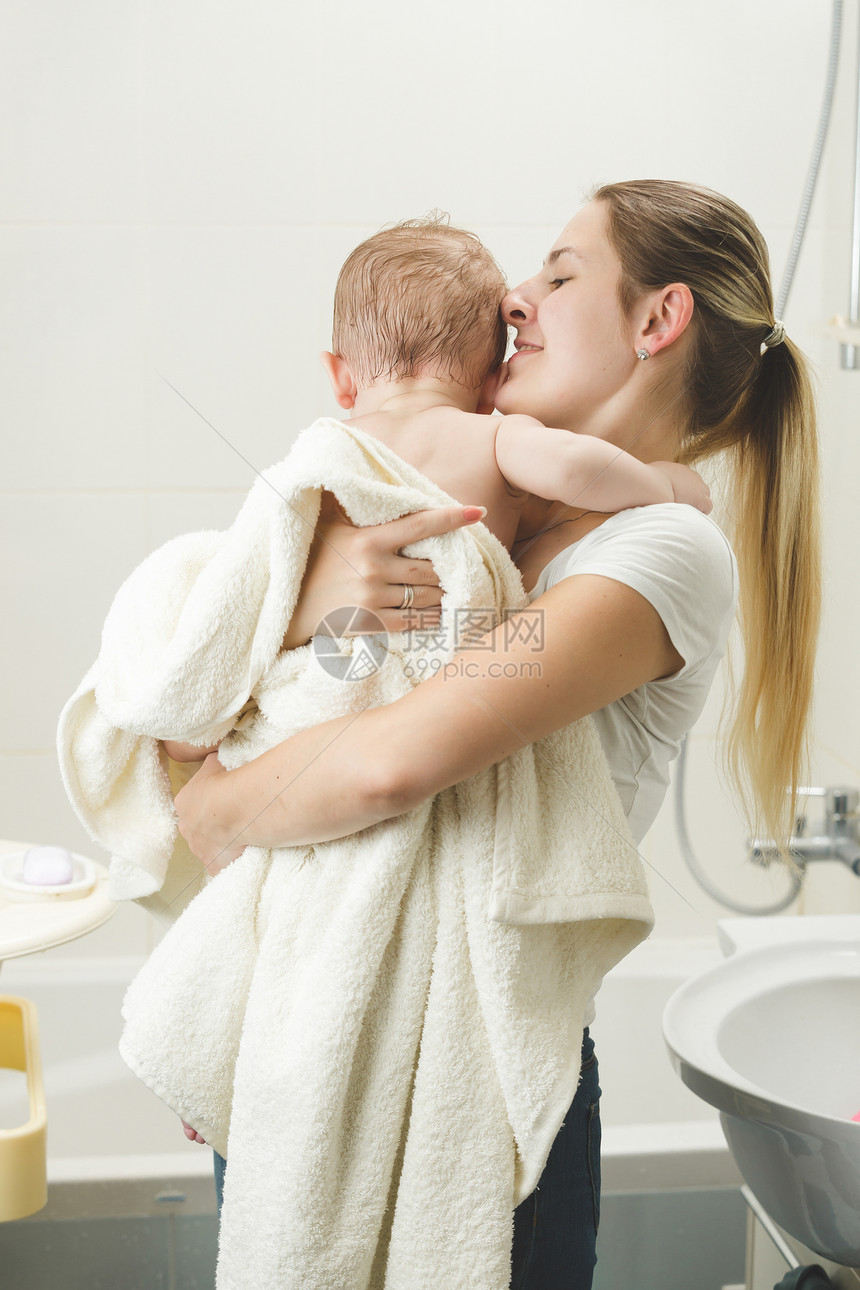 年轻母亲洗完澡后在浴室亲婴儿的肖像图片