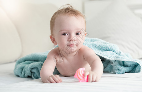 躺在蓝毛巾下床上并拿着塑料玩具的可爱婴儿肖像图片