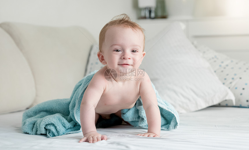 美丽的9个月大婴儿洗澡后穿着蓝毛巾爬在床上图片