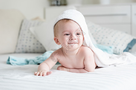穿着毛巾的可爱笑男孩洗完澡后在床上爬图片