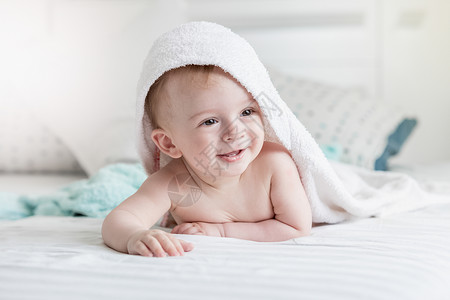 穿着毛巾的可爱笑婴儿肖像洗完澡后躺在床上背景图片