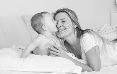 欢乐的母亲拥抱和吻在床上的婴儿男孩黑白像图片