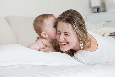 快乐的笑妈肖像和她孩子在床上玩耍图片