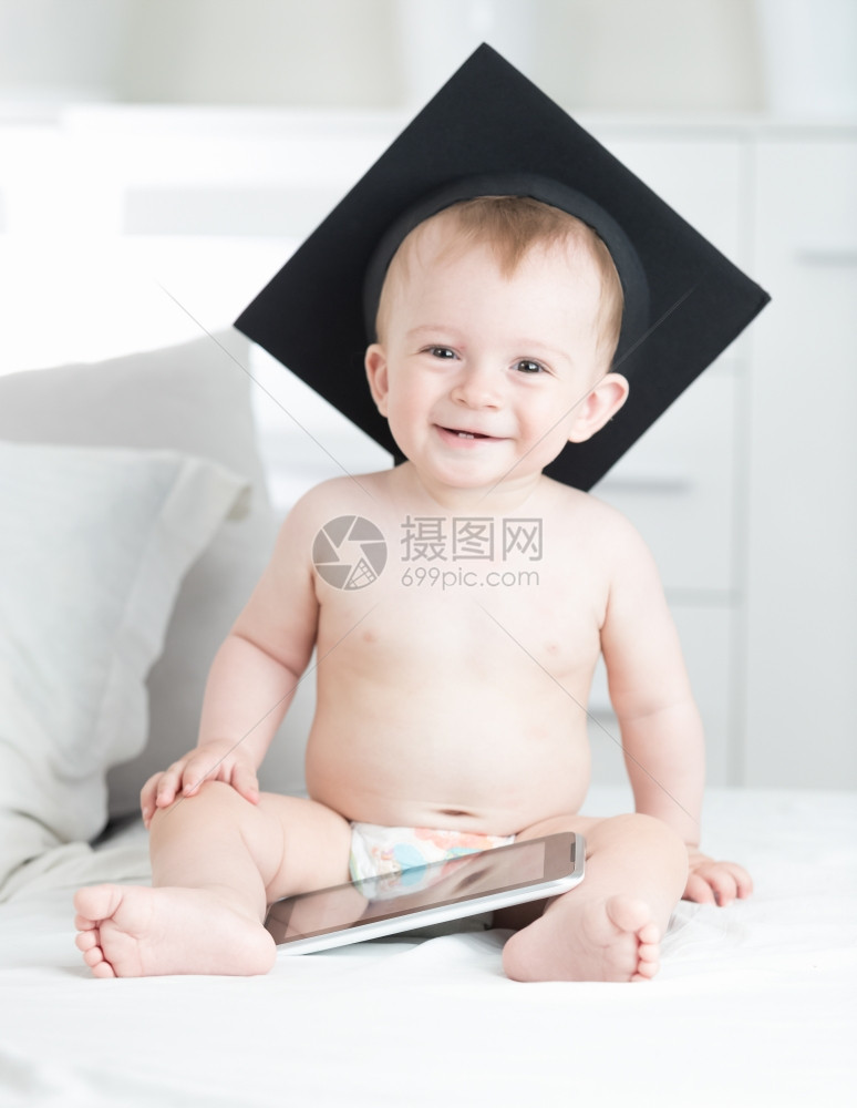 带着平板电脑坐在毕业帽上快乐笑的男孩肖像图片