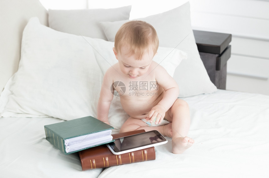 10个月大的婴儿男孩坐在一堆书的旁边并使用数字平板电脑图片