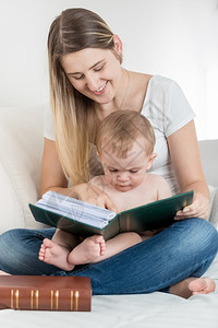 说书人美丽的笑母亲和9个月大的孩子男坐在沙发上看大书背景