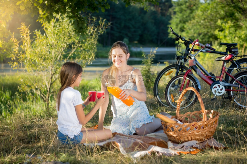 快乐笑的妈和女儿在野餐时喝橙汁图片