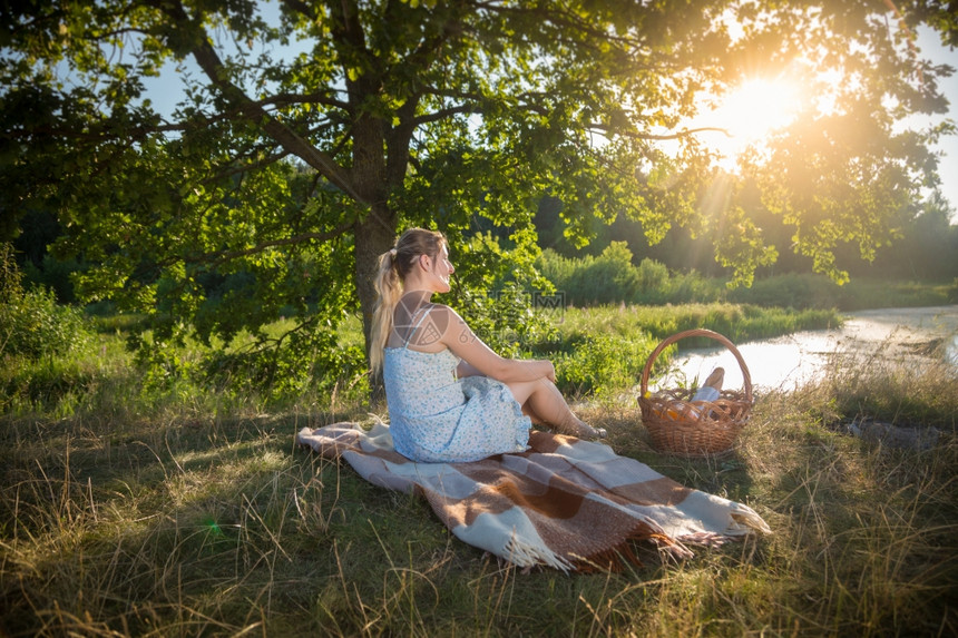 穿着裙子的漂亮女人在树下毛毯上放松看着日落图片