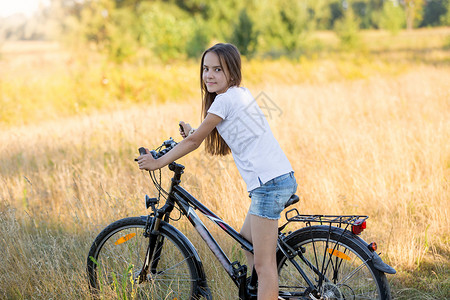 美丽的少女坐在草地骑自行车的肖像图片
