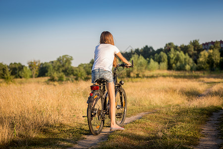 穿着短裤和T恤的漂亮女孩在草地上骑自行车图片