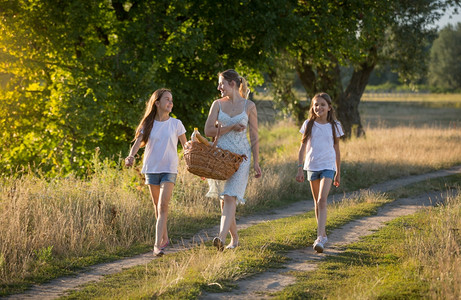 美丽的年轻母亲与女儿在日落时草地上散步图片