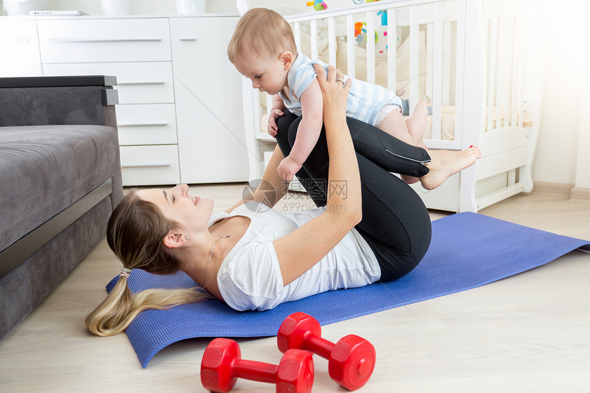 有婴儿的年轻母亲在客厅地板上做瑜伽锻炼图片