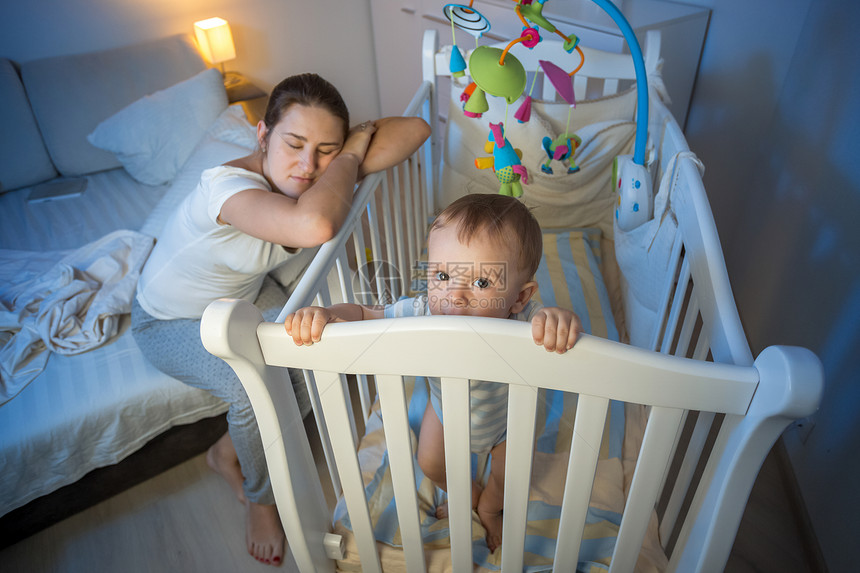 年幼的疲累母亲睡在婴儿床旁边图片