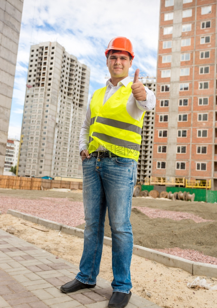 年轻笑的建筑工程师冒着大拇指在建筑工地上摆姿势图片