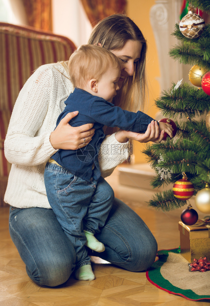 快乐的年轻母亲与她的10个月大婴儿男孩装饰圣诞树在活的罗姆图片