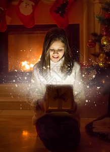 快乐女孩的肖像带着圣诞礼物打开盒子光闪的从盒子里出来图片