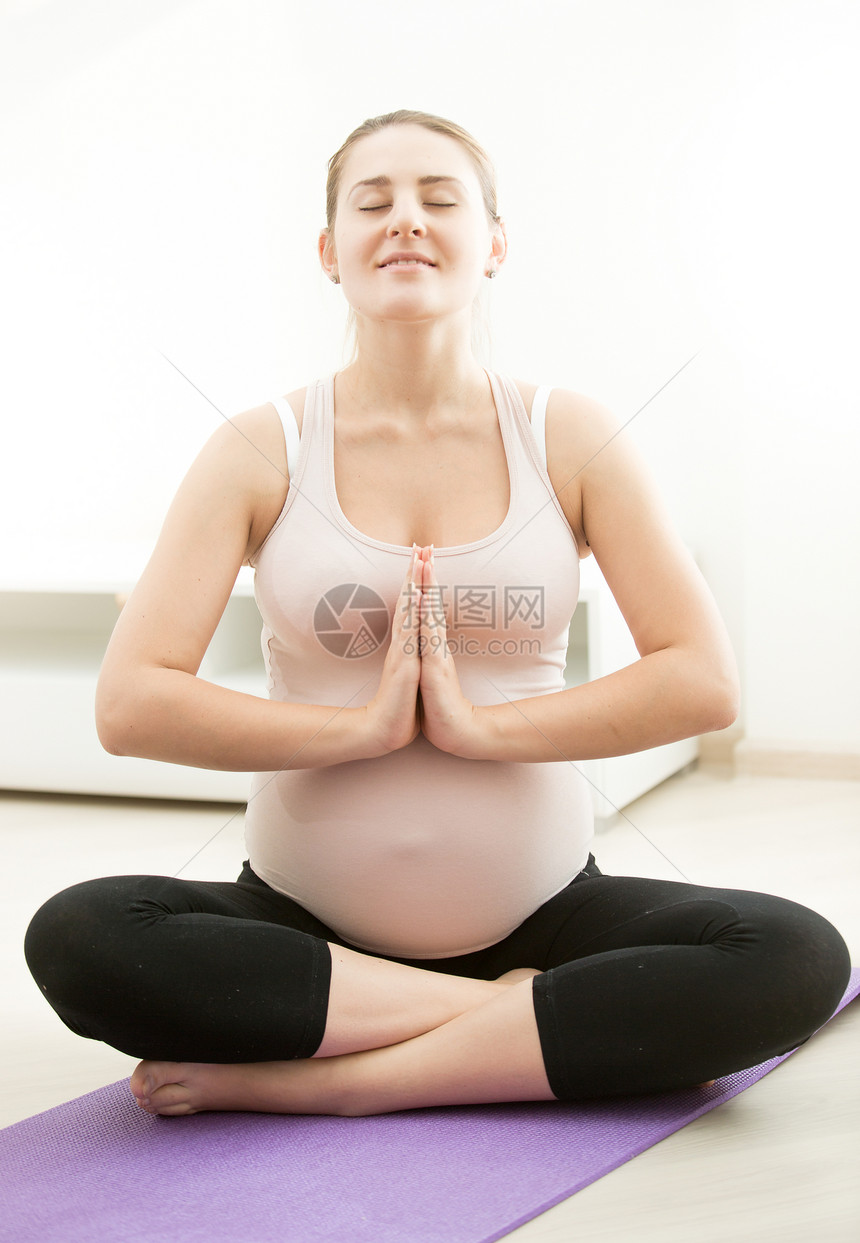 坐在健身席上并做瑜伽的微笑孕妇图片