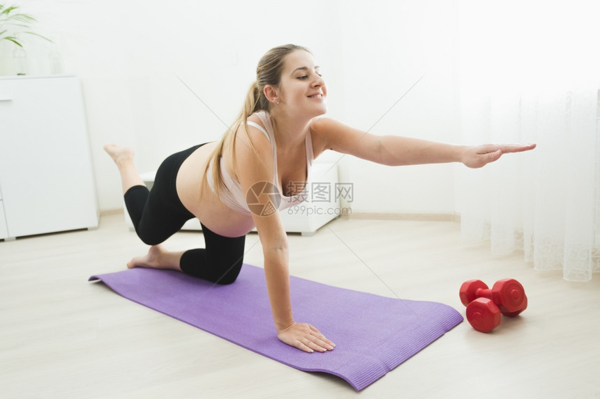 快乐的年轻孕妇在家健身席上运动和伸展图片