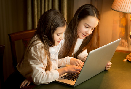 两个可爱的女学生晚上在笔记本做家庭作业图片