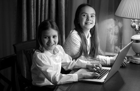 使用笔记本电脑拍摄两个小姐妹的黑白画像图片