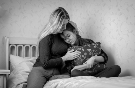 年轻母亲在床上安慰十几岁女儿的黑白年轻母亲肖像图片